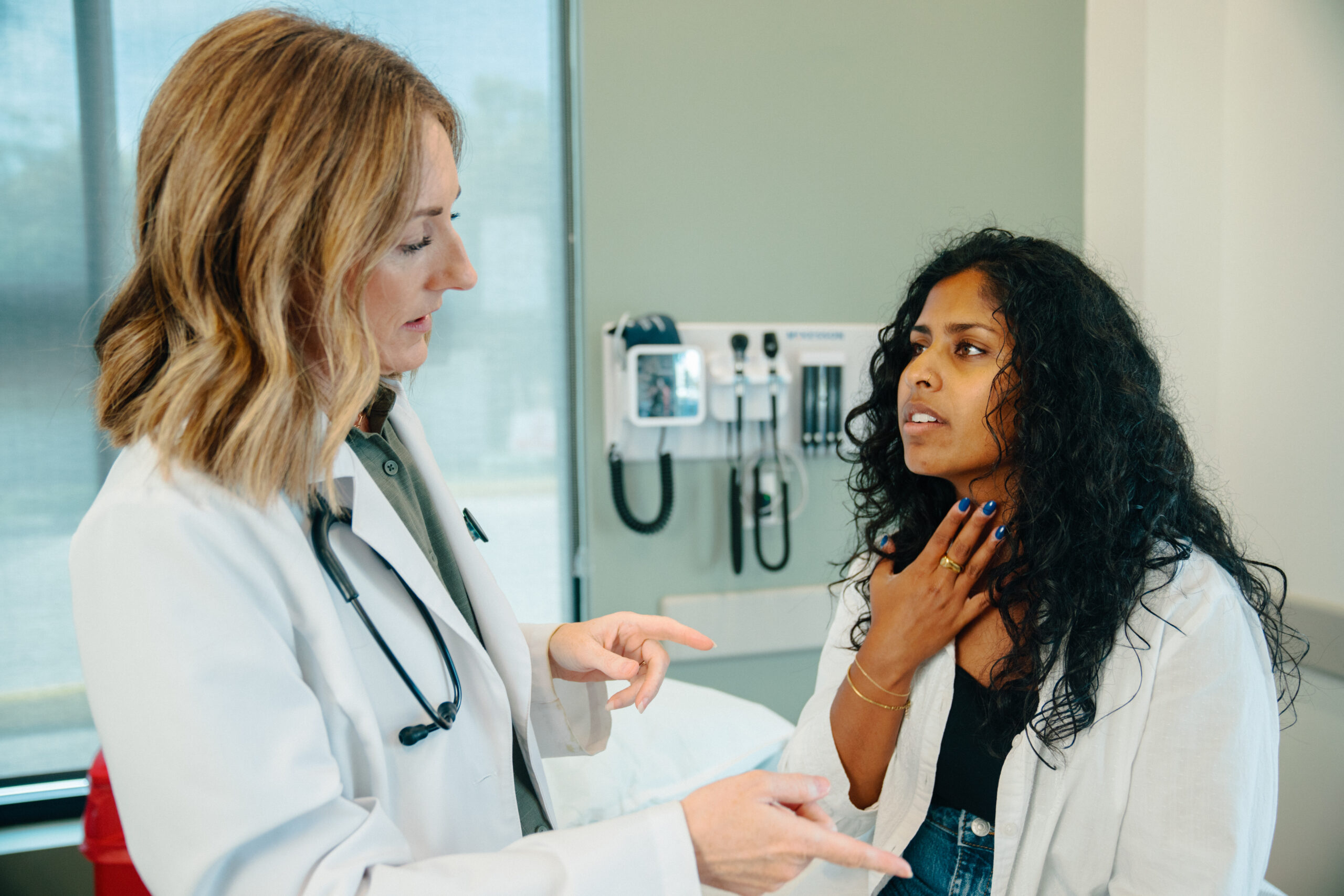 Patient points to her neck gesturing to her strep throat pain to her female provider